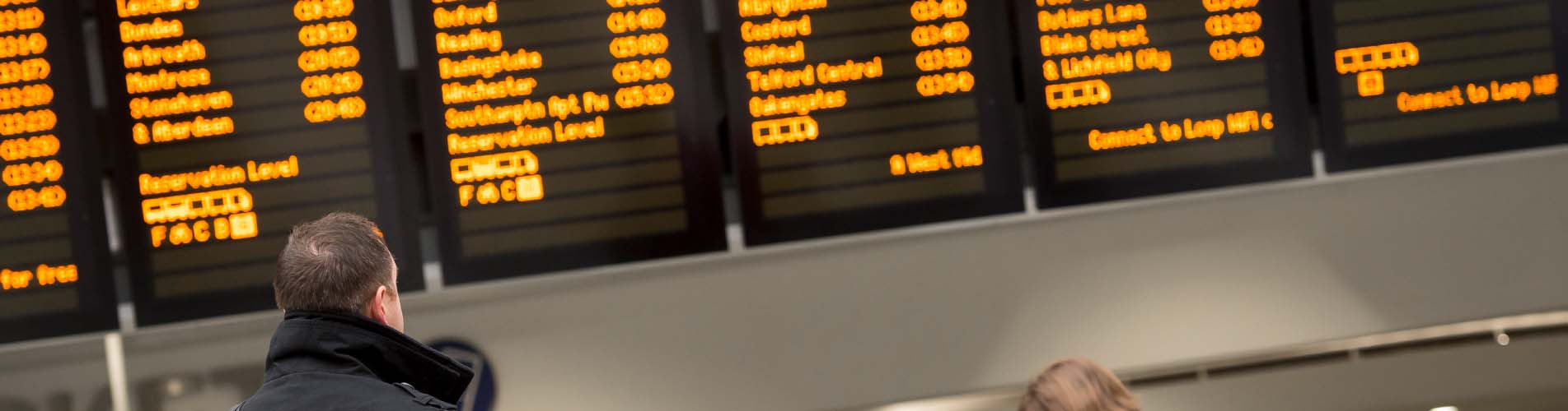 Passengers checking a train information board at a British railway station.