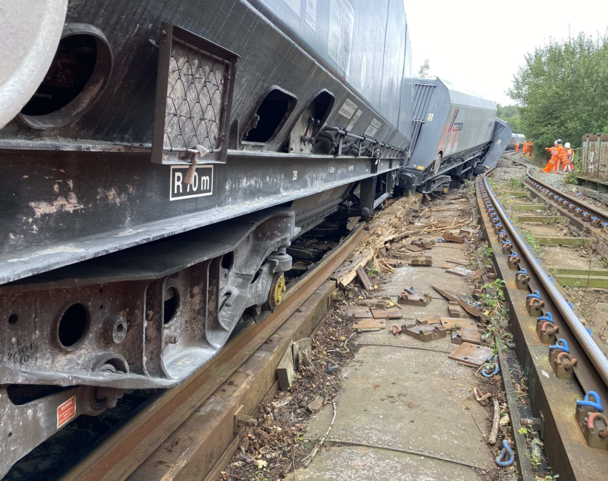 Partially derailed freight train at Audenshaw with a group of railway workers assessing the scene.