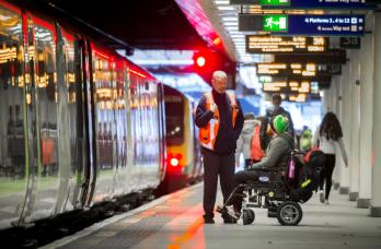 Wheelchair user in a railway station platform being assisted by a member of staff