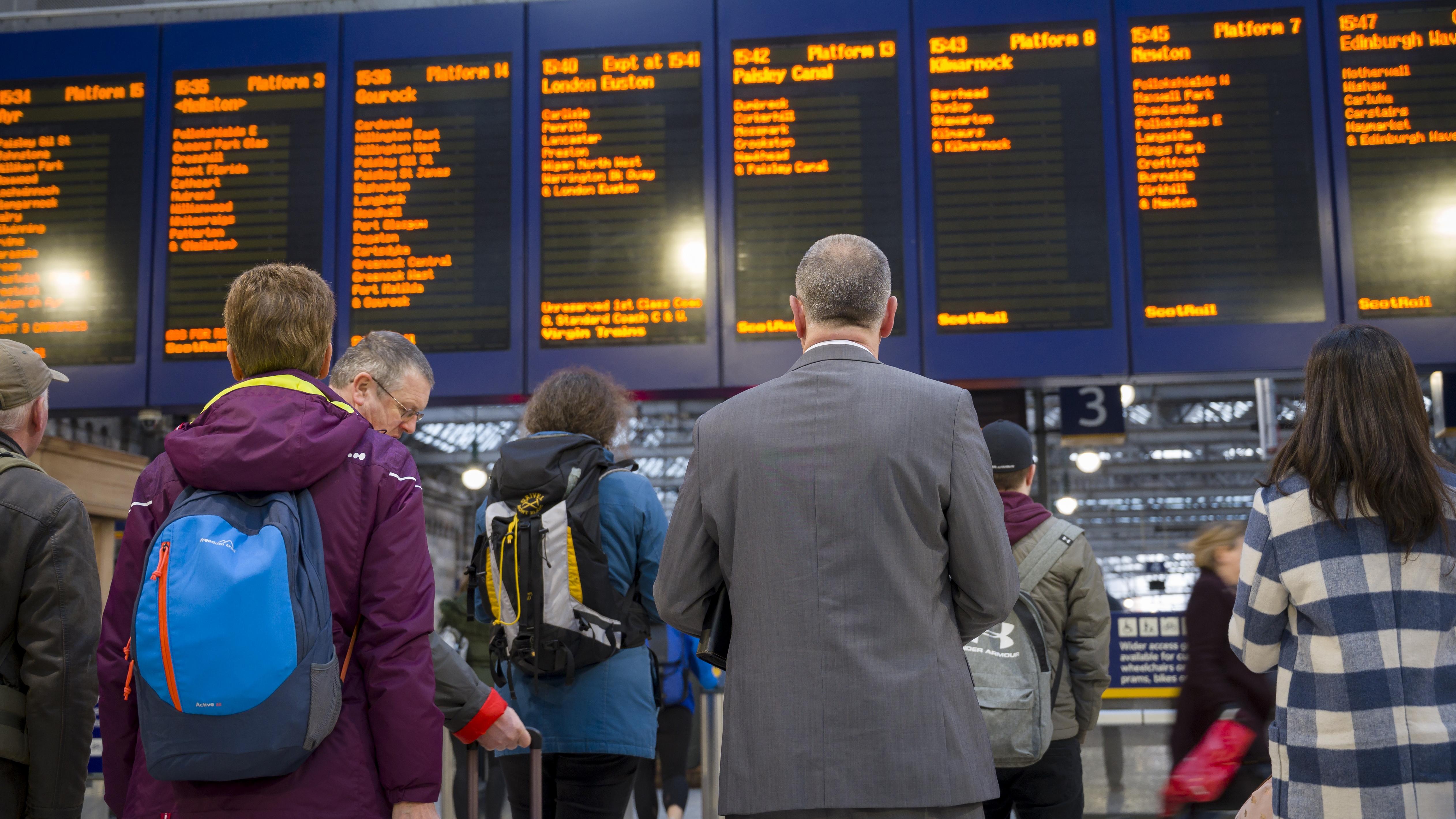 An image of rail passengers staring at a service board at a railway station.