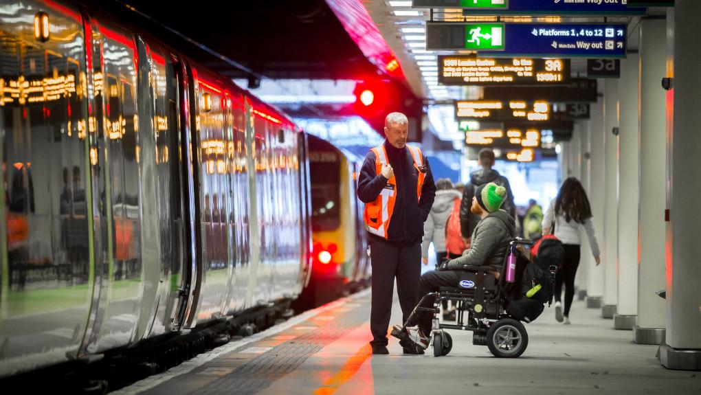 Wheelchair user in a railway station platform being assisted by a member of staff