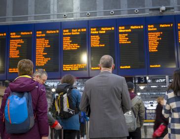 An image of rail passengers staring at a service board at a railway station.